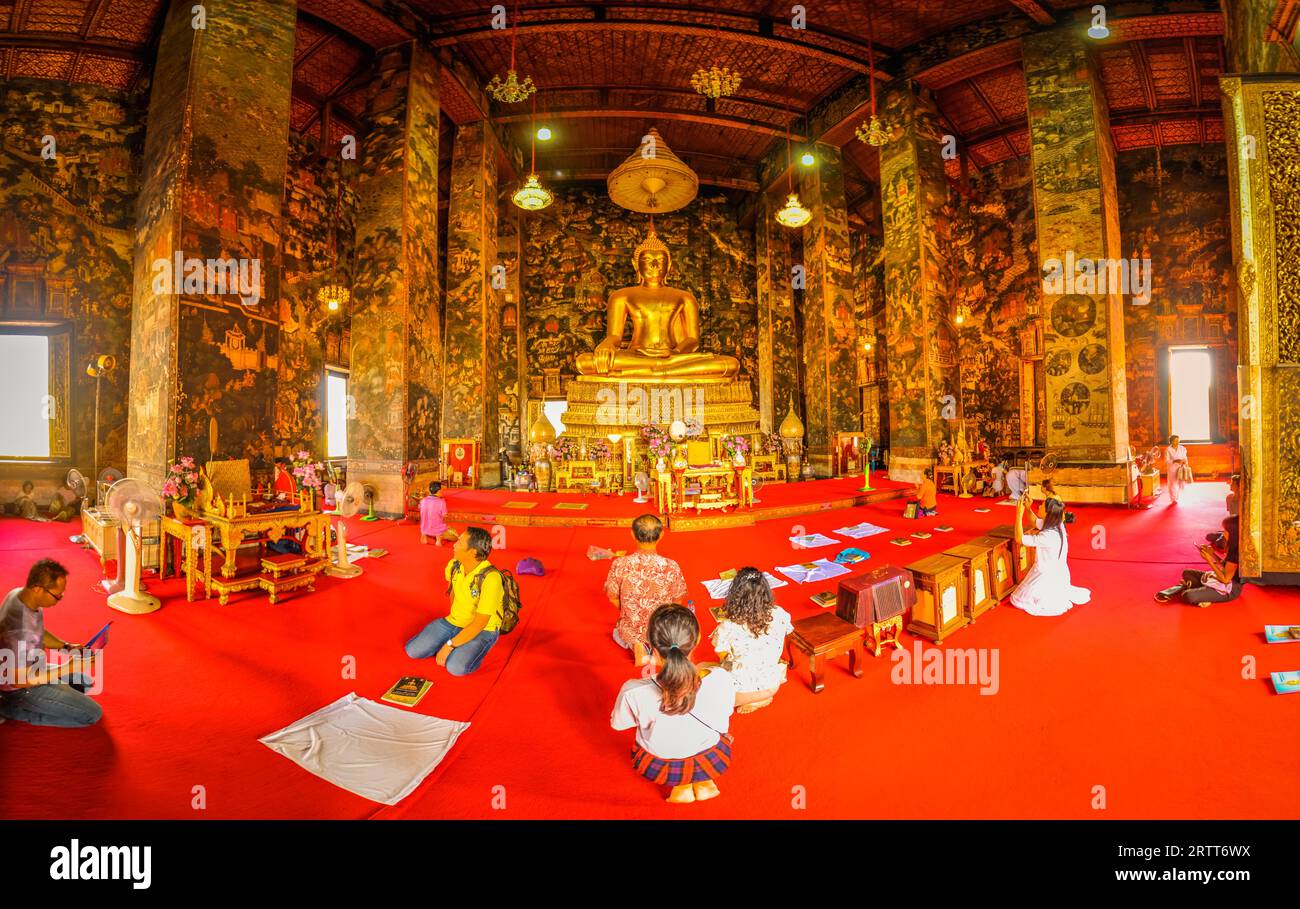Photo of people kneeling on ground in front of big statue of Buddha in temple Suthat Wat in Bangkok, Thailand Stock Photo