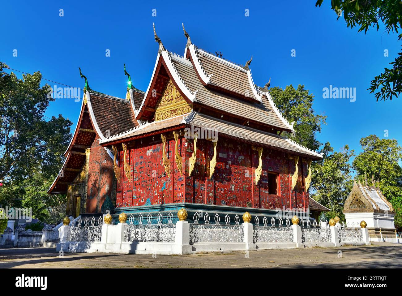 Wat Xieng Thong, the temple with intricate coloured glass mosaic on a stunning red wall amidst a clear blue sky, Dec 2014, Luang Prabang, Laos Stock Photo