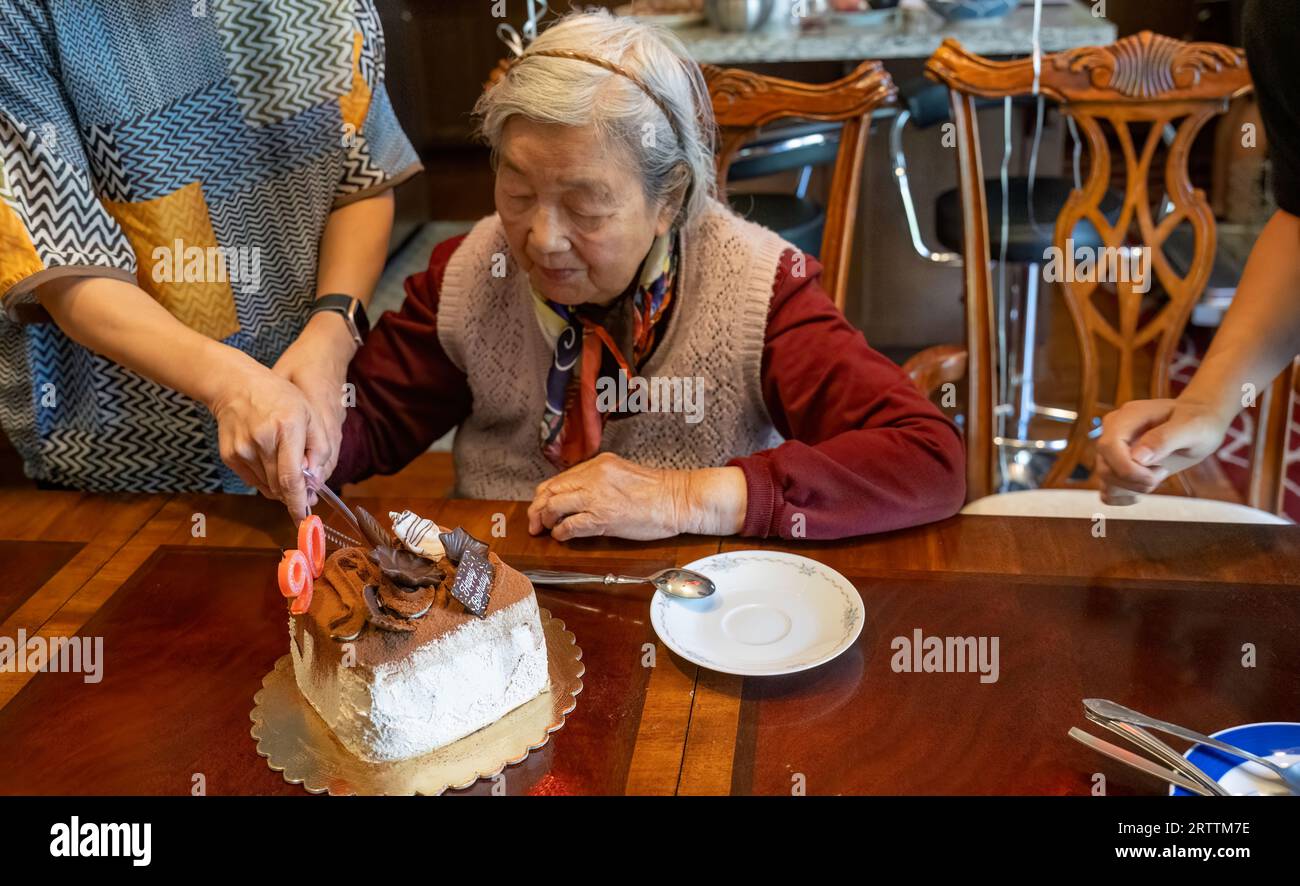 Senior woman cutting cake with the help of daughter. Celebrating 90th birthday with a cake with number 90 candles on. Stock Photo