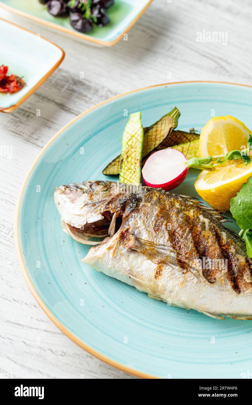Grilled sea bream with vegetables and greens on wooden table Stock Photo
