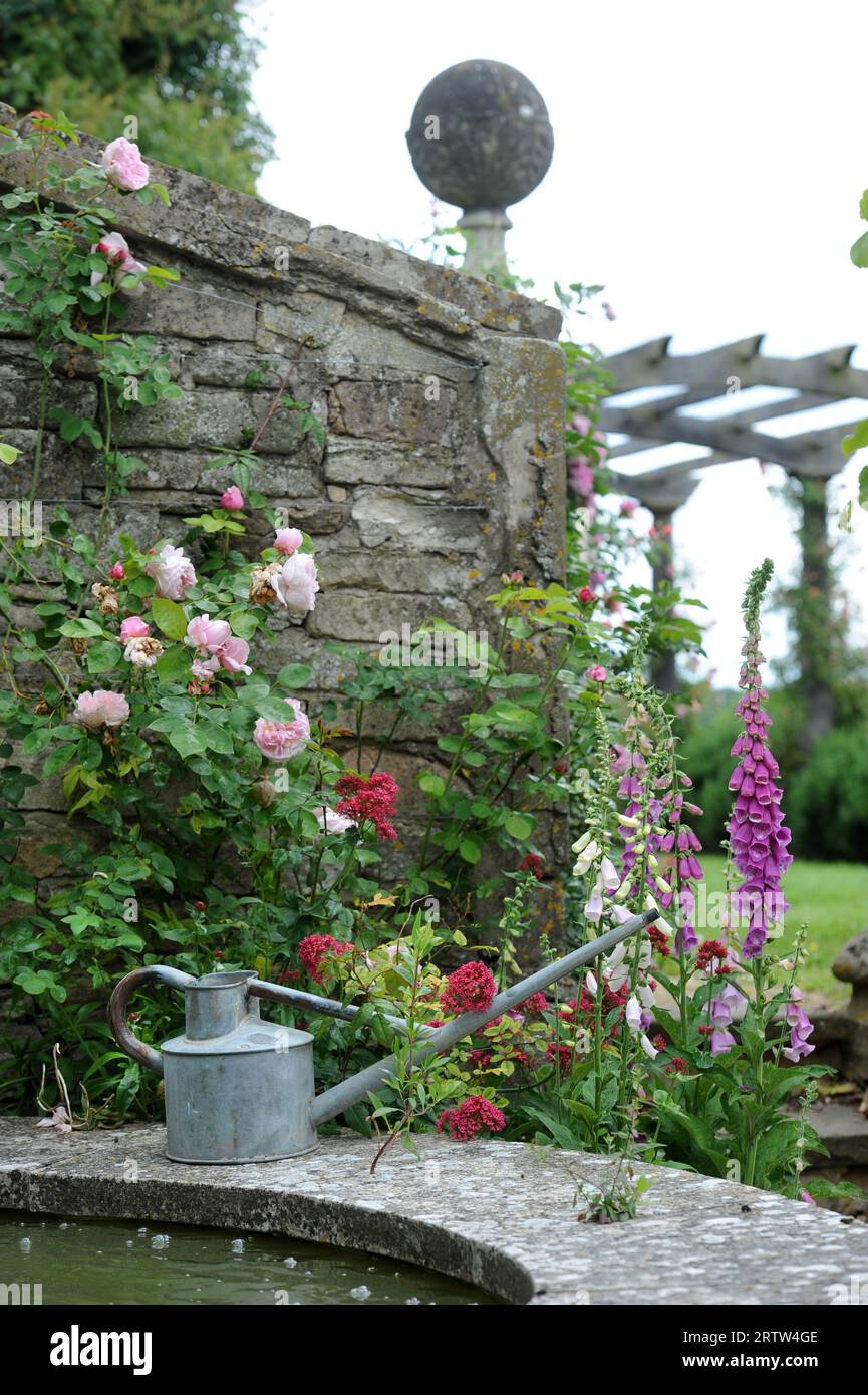 Watering can by a water feature in a walled garden, UK Stock Photo Alamy
