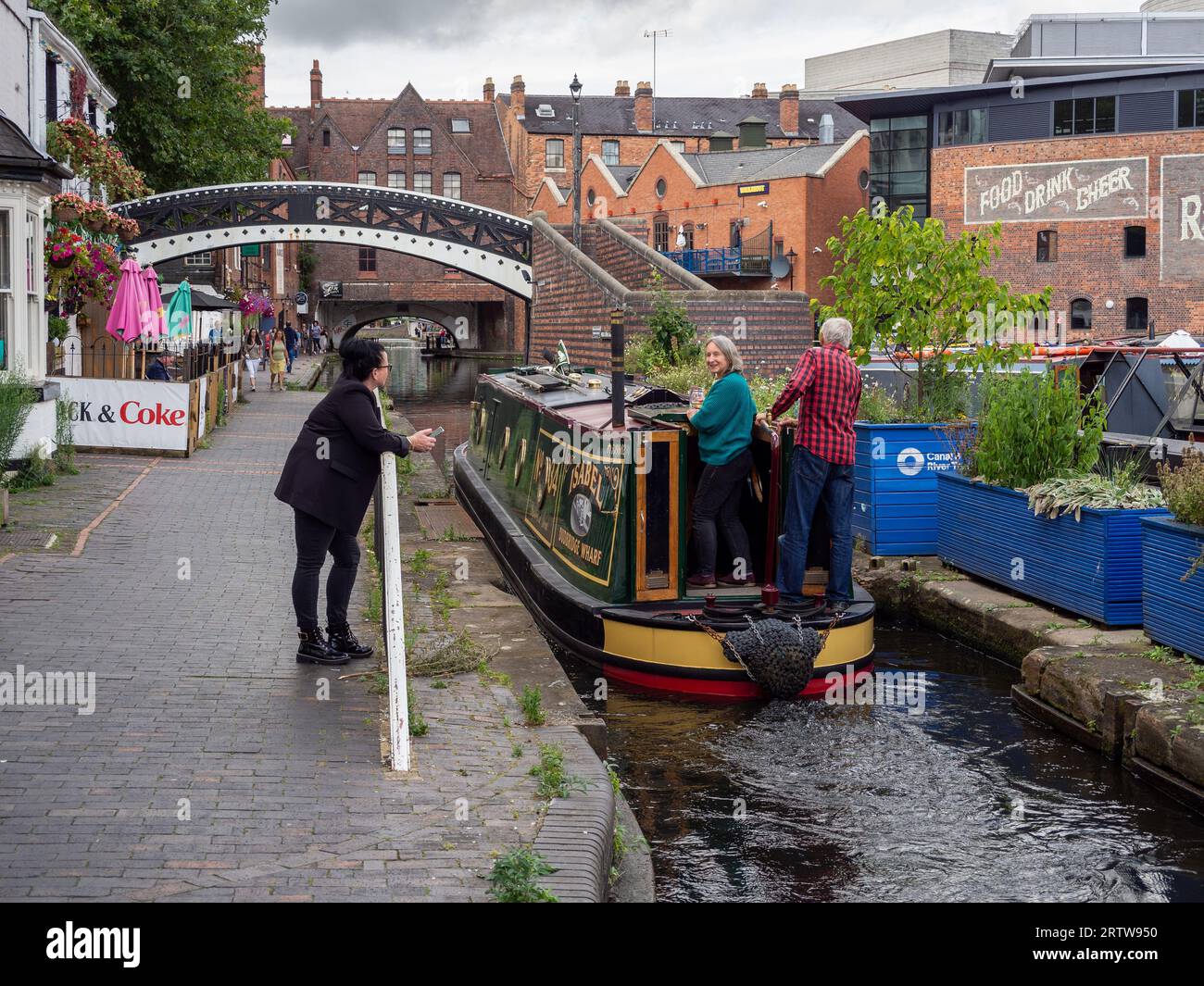 A female bystander chats with two bargees on a narrowboat as they pass through Gas Street Basin, Birmingham, UK Stock Photo