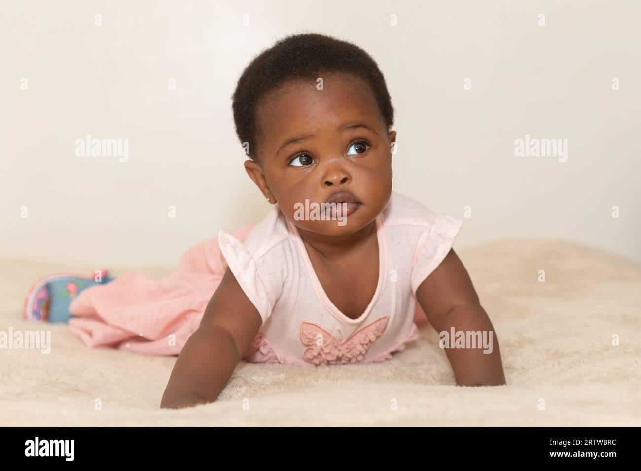 Portrait of a black baby girl with a serious expression dressed in pink crawling on a bed Stock Photo