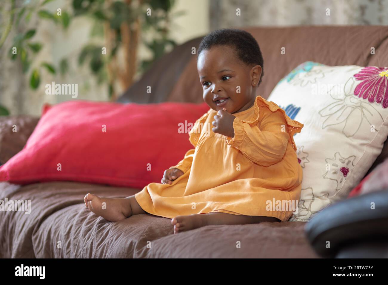 Portrait of a smiling black baby girl dressed in an orange dress sitting on a couch Stock Photo