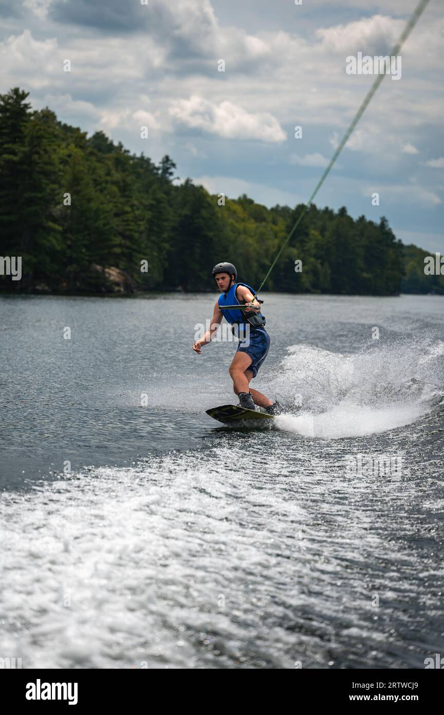 Teenage boy wakeboarding from boat on lake on summer day. Stock Photo