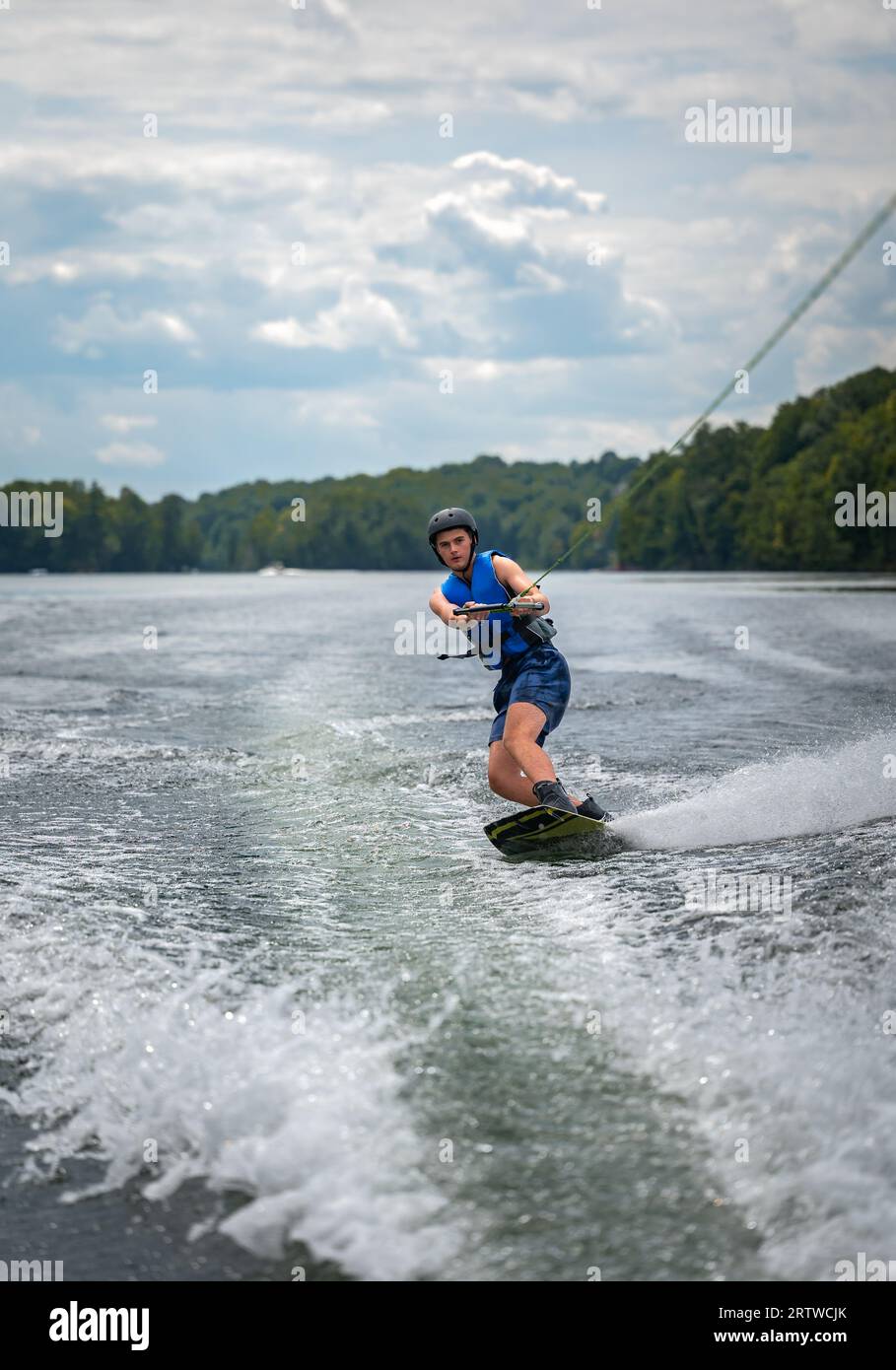 Teenage boy wakeboarding from boat on lake on summer day. Stock Photo