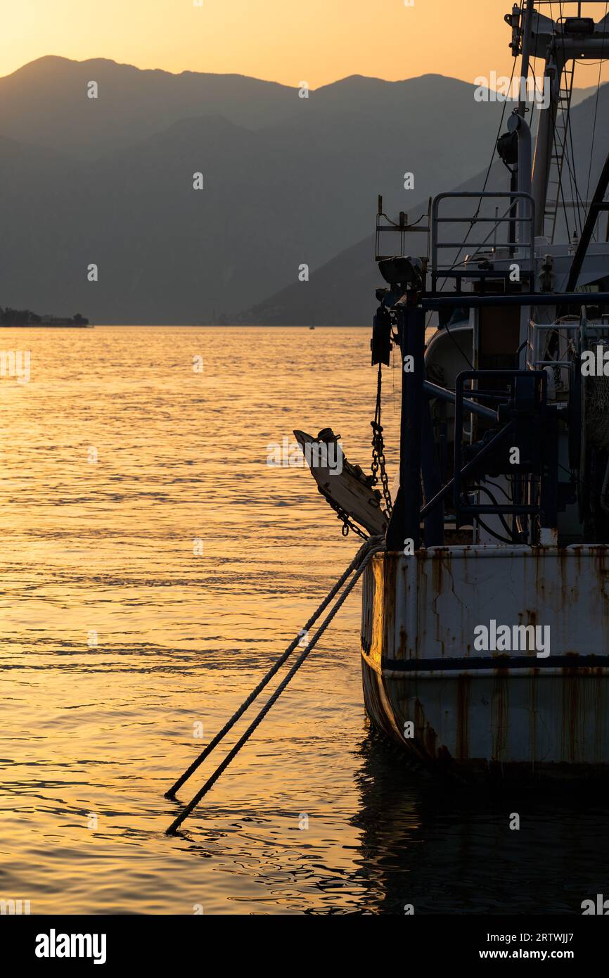 An old, weathered, rusty fishing boat is anchored in the bay at sunset ...