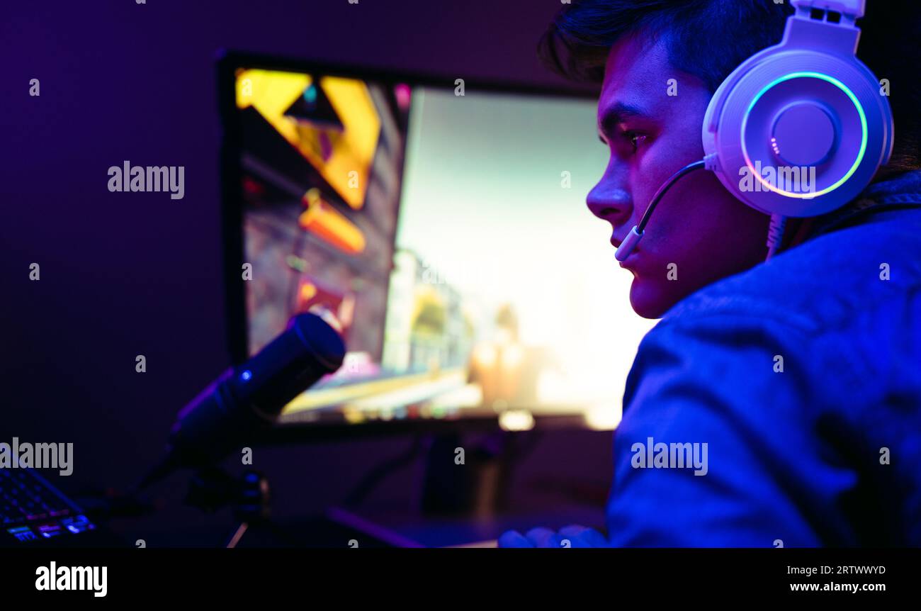 Video game player getting into the gaming world as he settles into his computer setup, with a microphone in front of him. Man delivering a gameplay br Stock Photo