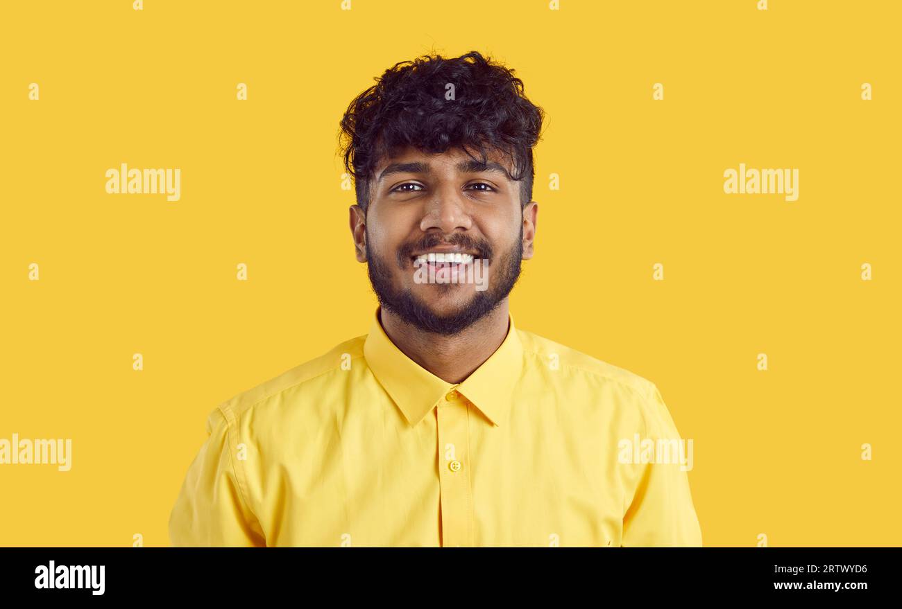 Young happy ethnic Indian man millennial with beard and curly hair stands on yellow background Stock Photo