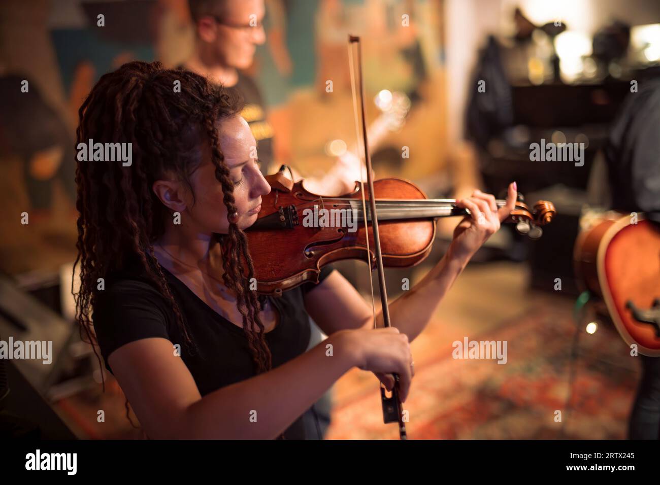 A female violinist plays the violin. Band performs on stage, rock music