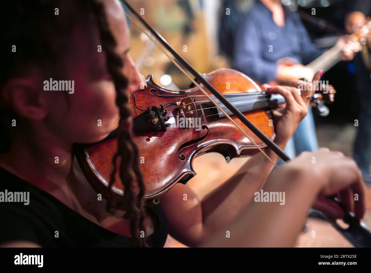 A female violinist plays the violin. Band performs on stage, rock music