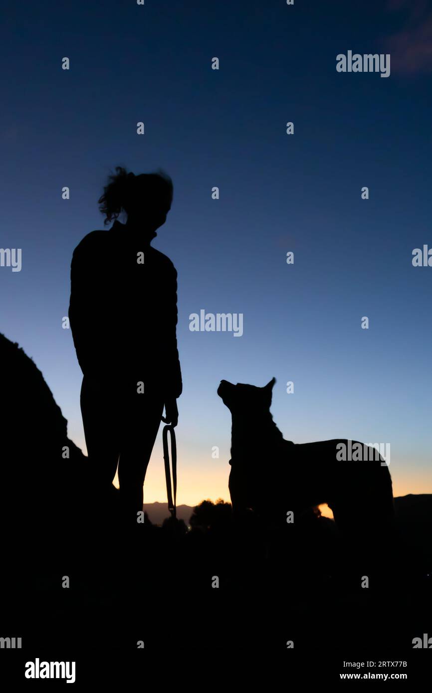 Young woman and her dog on a hike at sunrise in silhouette Stock Photo