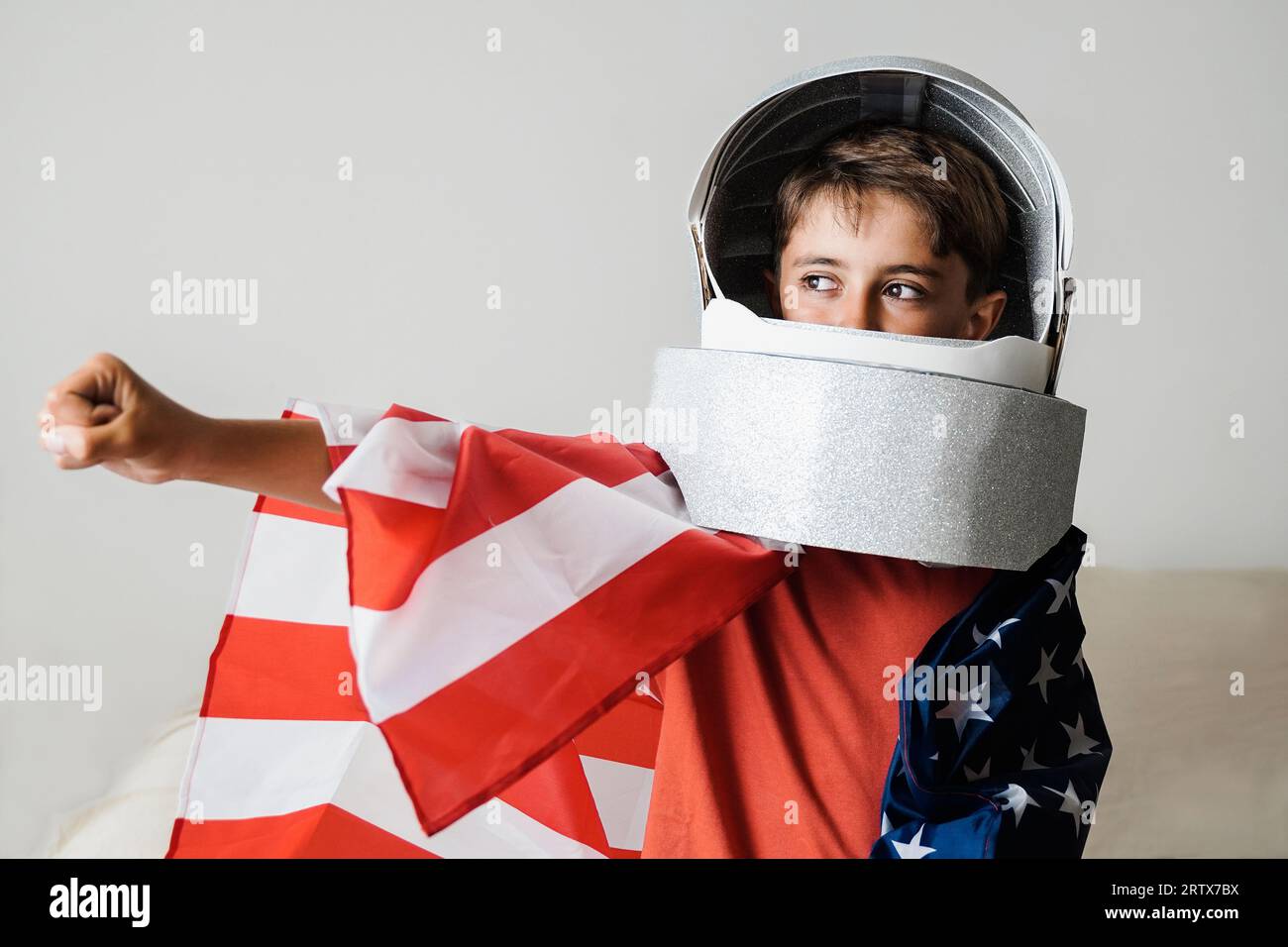 Astronaut kid playing with crafty helmet toy and wearing US American flag - Future spaceman dreaming and having fun at home Stock Photo