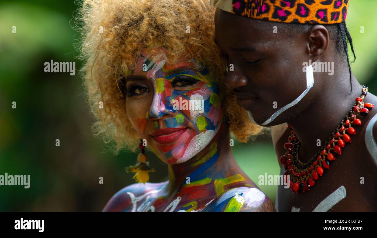 Nueva Loja, Sucumbios / Ecuador - September 3 2020: Portrait of black couple in love with color painted body hugging in a forest with unfocused green Stock Photo