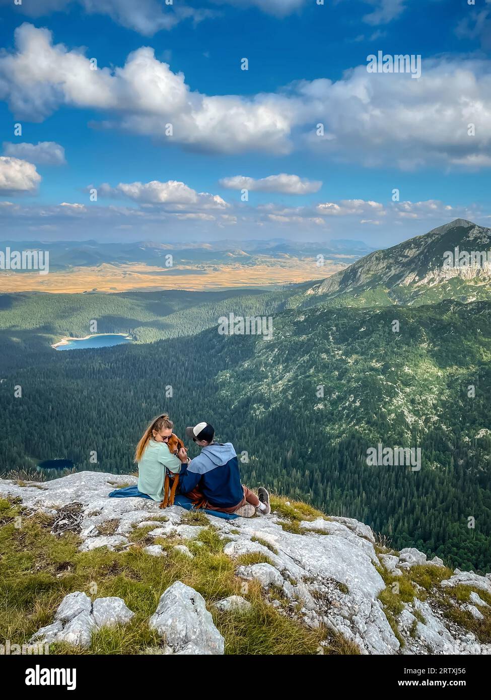 Young Couple with Dog Sitting on Mountain Top Stock Photo - Alamy
