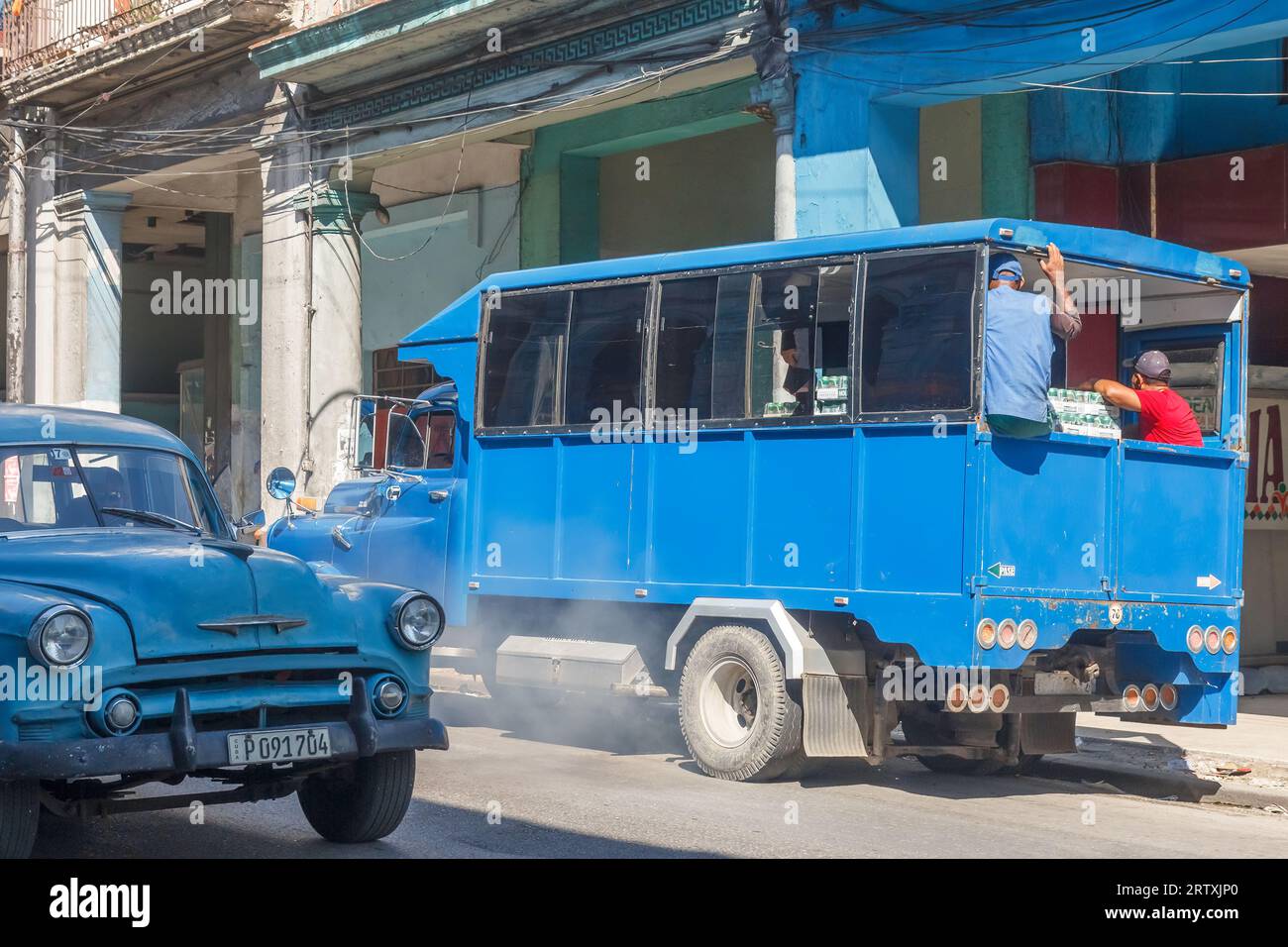 Havana, Cuba, 2023, Cuban people transport beer cases on an old truck. A vintage car drives in the opposite direction. Stock Photo