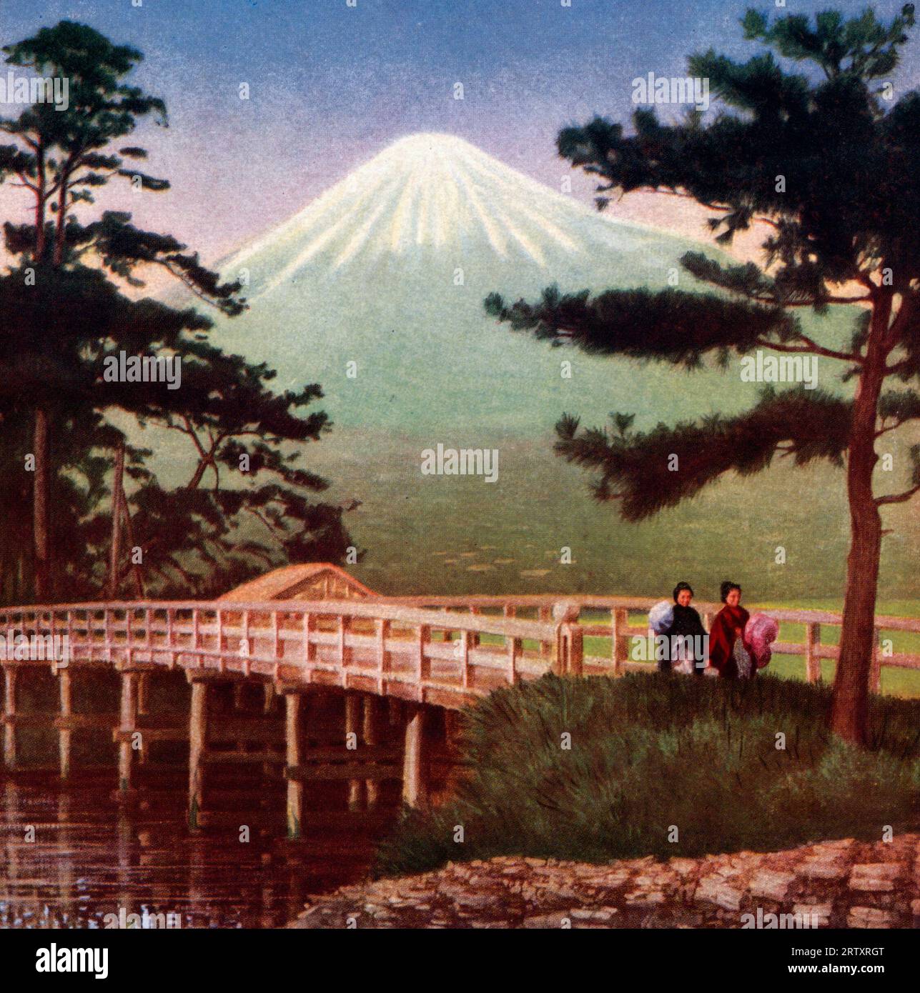 Japanese couple walking over a footbridge with Mount Fuji in the background, circa 1910 Stock Photo