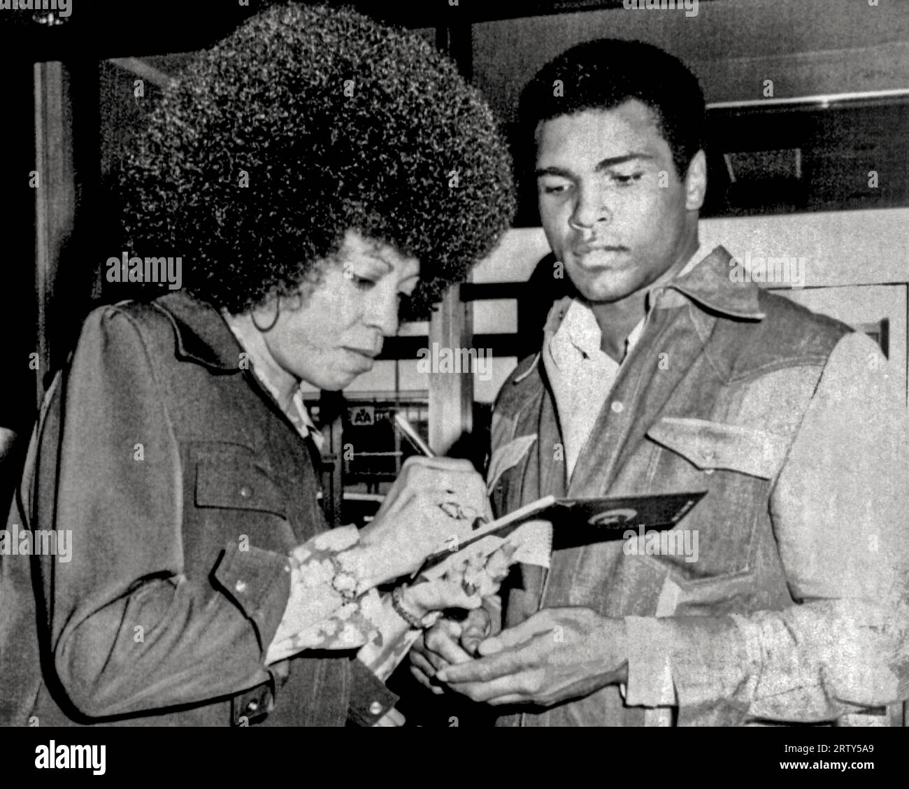 New York, New York  September 9, 1974 Muhammad Ali and Angela Davis exchange autographs when they run into each other at La Guardia Airport. Ali was on his way to Zaire to fight George Foreman, Stock Photo