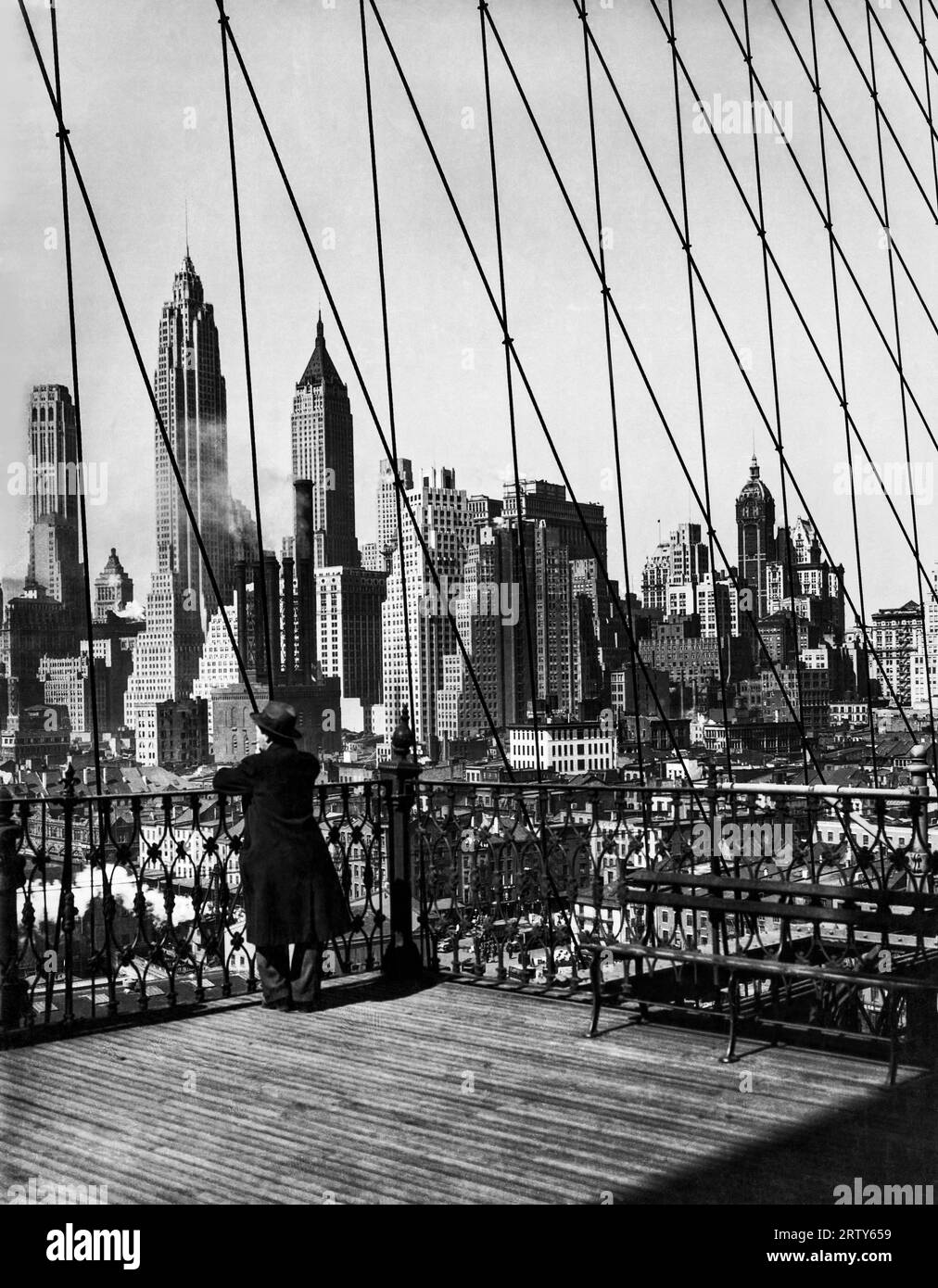 New York, New York    c. 1933 The Lower Manhattan skyline with its new additions of the City Bank Farmers Trust, the Cities Service, and the Bank of Manhattan buildings, as seen through the cables of the Brooklyn Bridge over the East River. Stock Photo