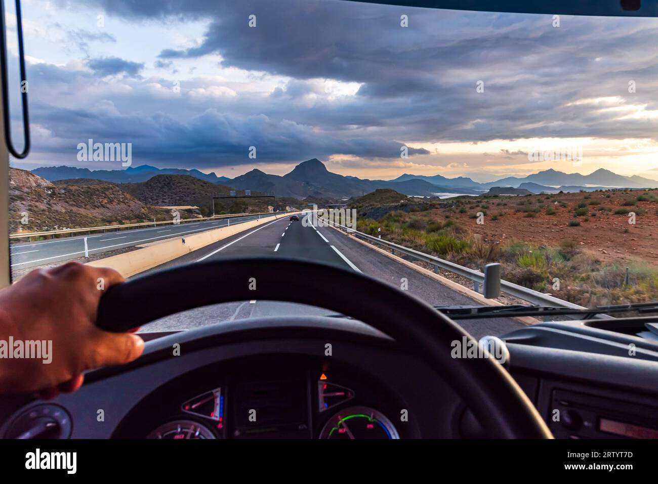 View from the driving position of a truck of the highway and a landscape of mountains in the background at dawn. Stock Photo