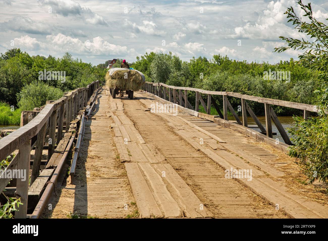 village scene with old horse cart carrying hay over a wooden bridge Stock Photo