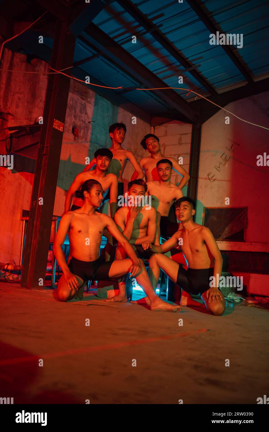a group of men without clothes dancing poses in an old building with a red light at night Stock Photo