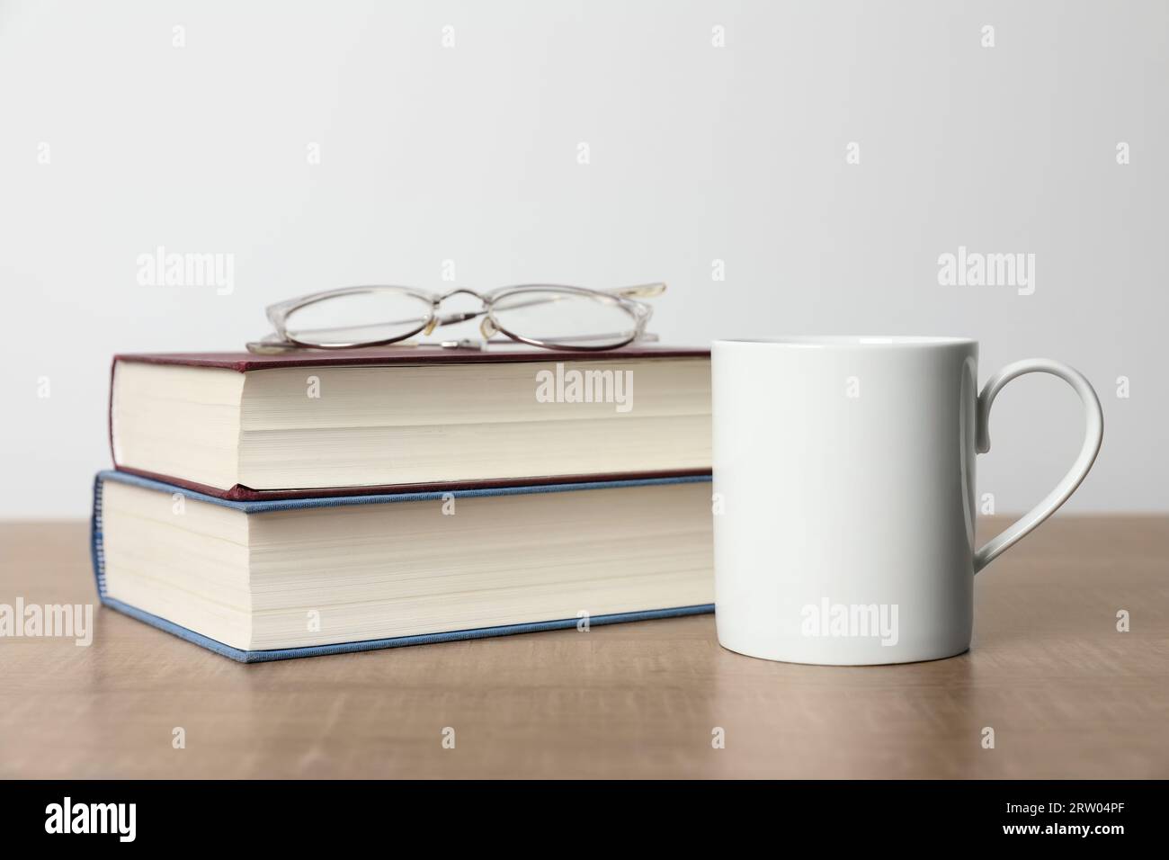 White ceramic mug, stack of books and glasses on wooden table Stock Photo