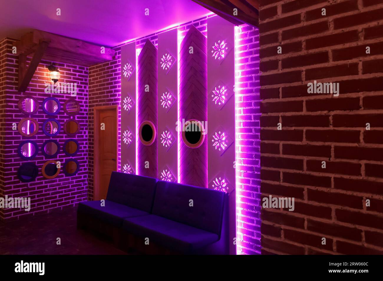 Decorative interior design element with brick walls, mirrors, sofa and neon pink light. Stock Photo