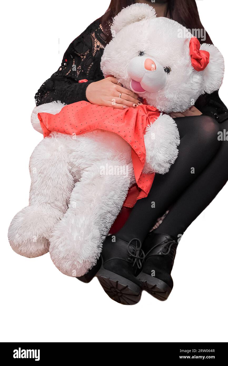 A girl in black clothes in a sitting position holds a large soft white toy of a fluffy bear girl on an isolated background. Stock Photo