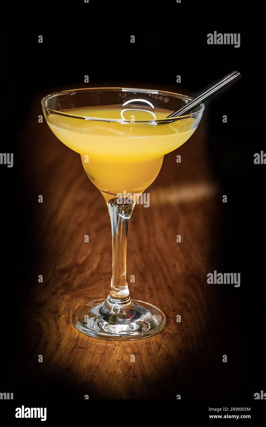 Cocktail alcoholic glass with orange juice and a straw stands on the bar counter on a dark background vignette. Stock Photo