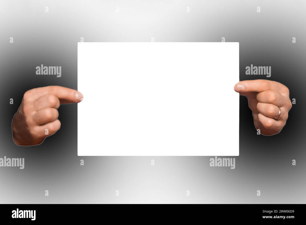 Man holding a sheet of A4 paper in their hands, an empty space for text and design blank white on a dark background. Stock Photo