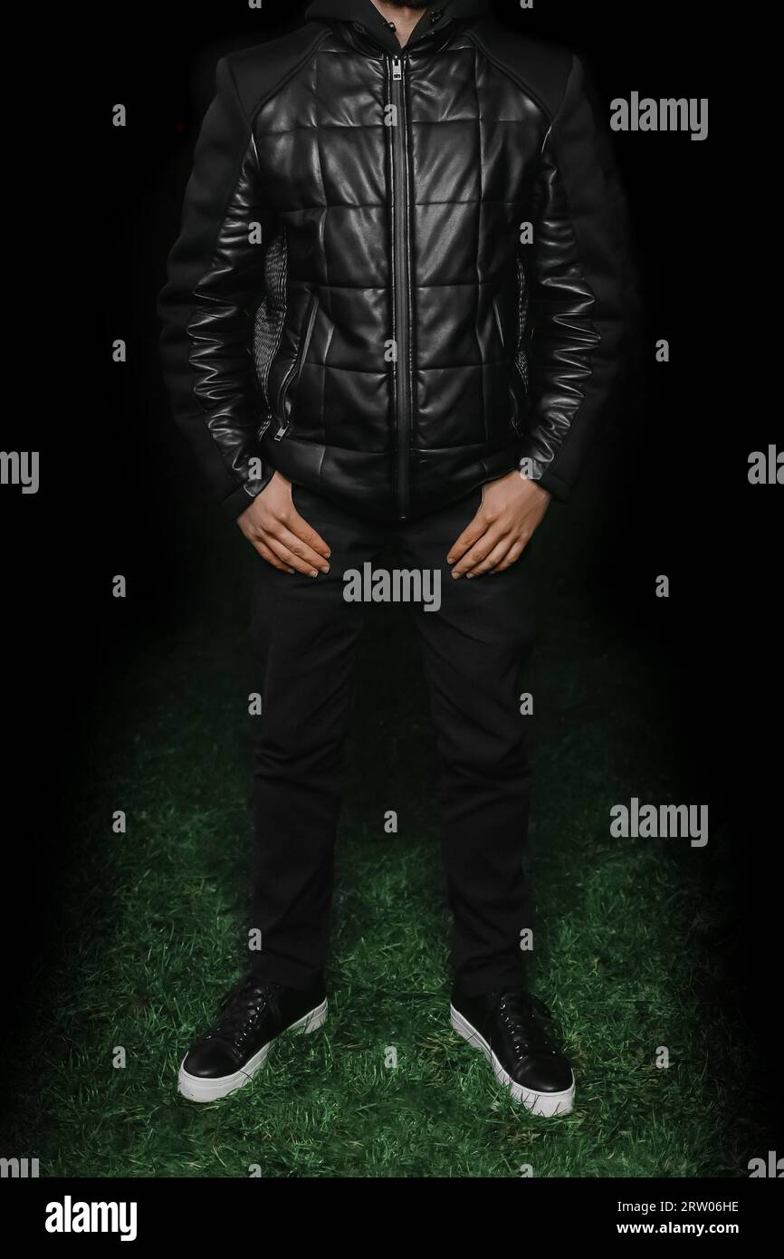 Men's fashionable style of clothing black twist, pants and sneakers posing with hands in pockets against the dark background of the outdoor. Stock Photo