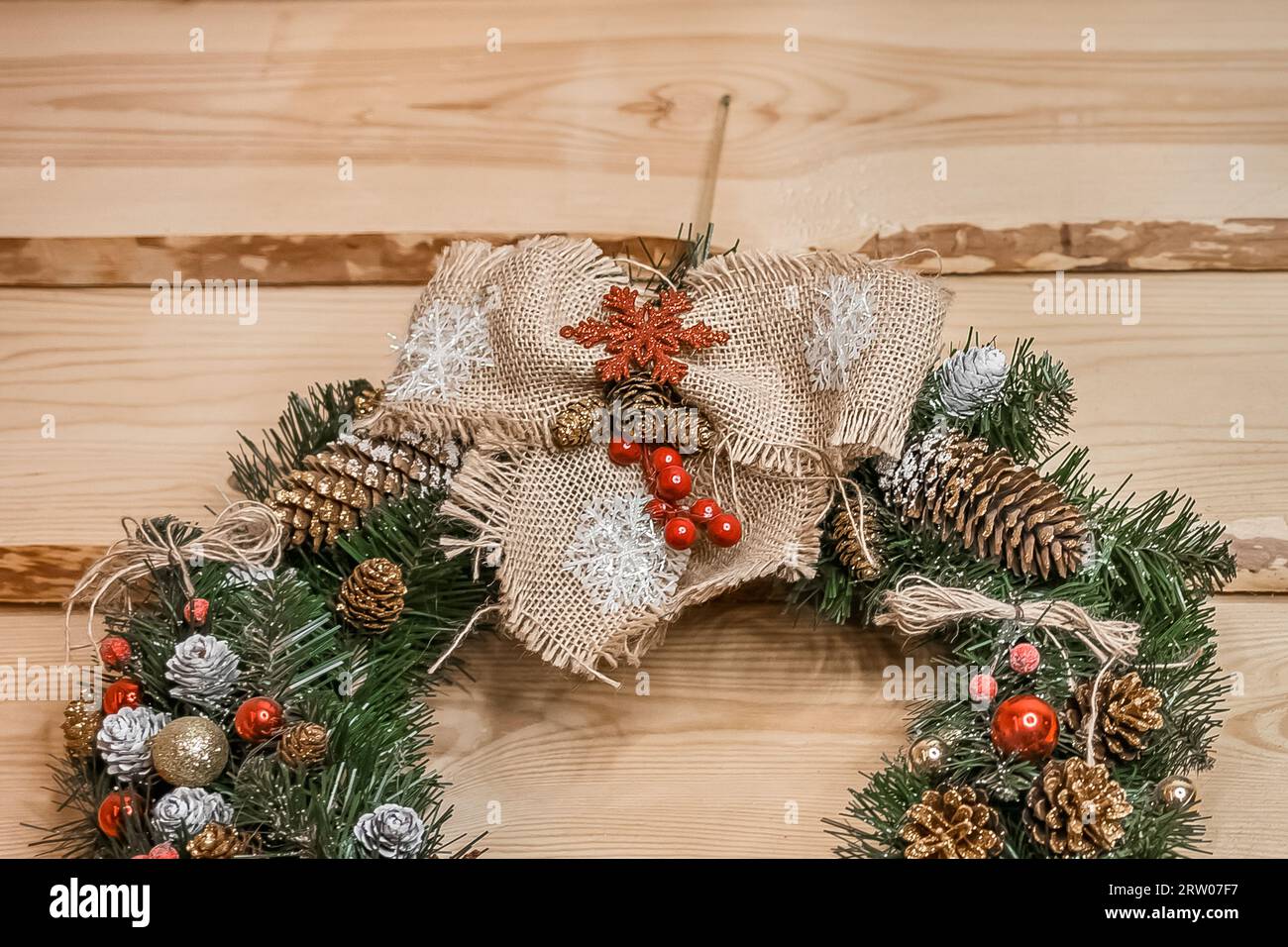 Christmas wreath made of artificial spruce, pine needles, decorated with cones and toys on a wooden background, close up. Stock Photo