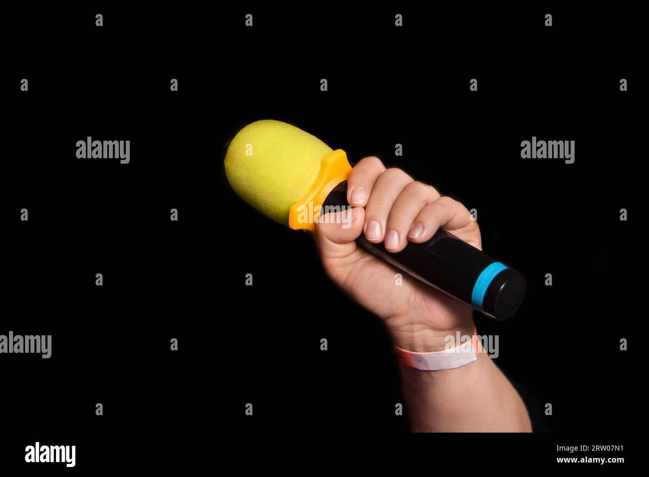 Female person hand close-up holding microphone professional karaoke singing equipment on black background. Stock Photo