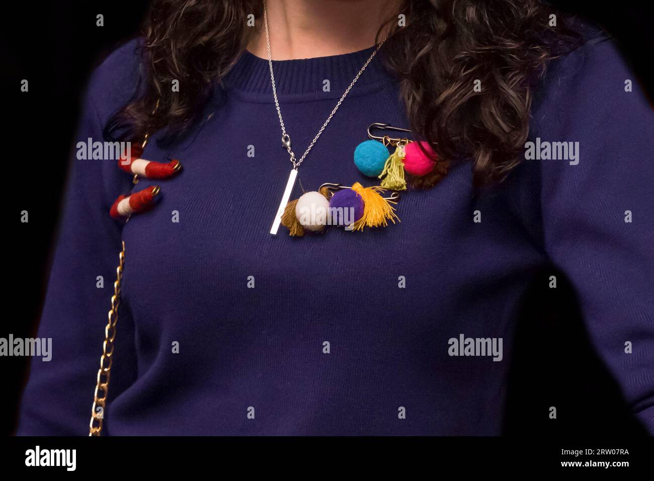 Women's dark purple sweater decorated with colored objects, soft toys on a pin, close-up on a black background. Stock Photo