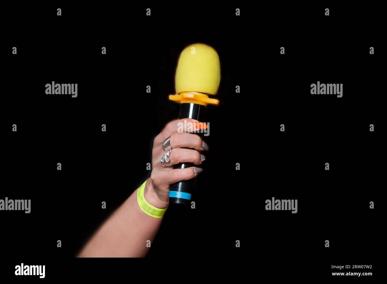 Female person hand close-up holding microphone professional karaoke singing equipment tool on black background. Stock Photo