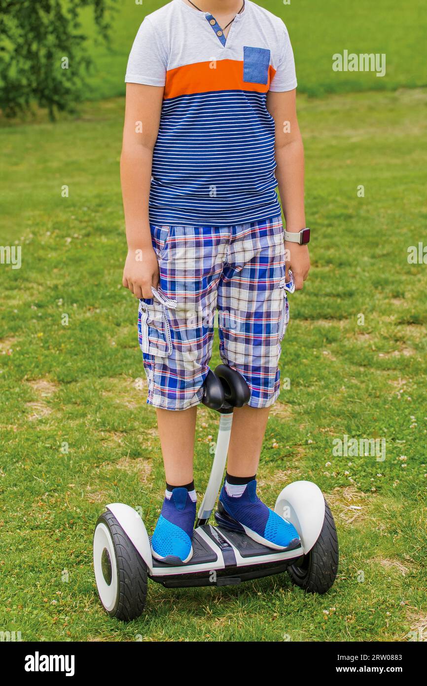 A boy portrait in a T-shirt and sneakers, stands on a hoverboard in a park on the street. Stock Photo