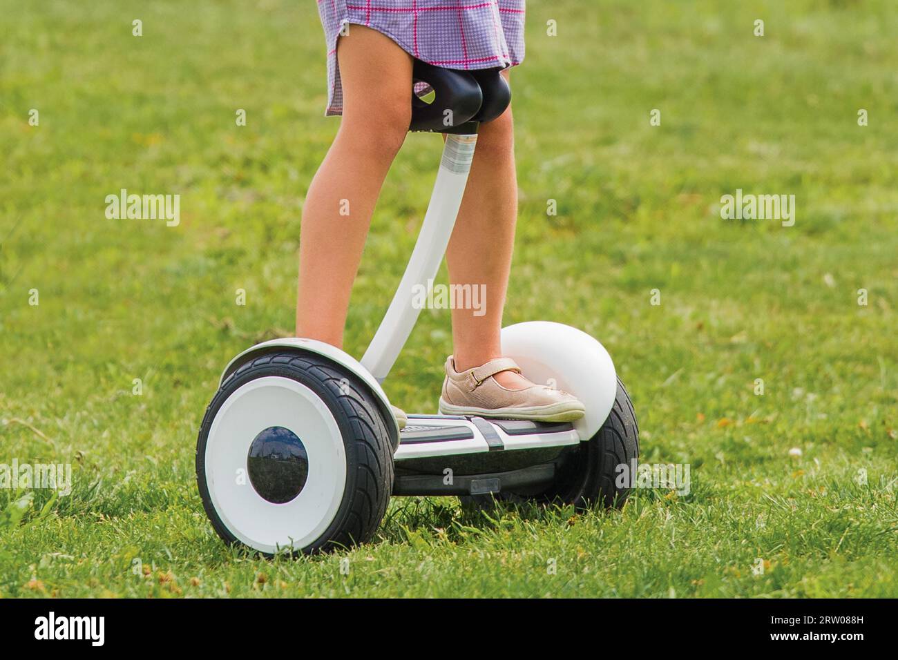 The girl's legs stand and ride on a hoverboard against the background of the grass of the park. Stock Photo