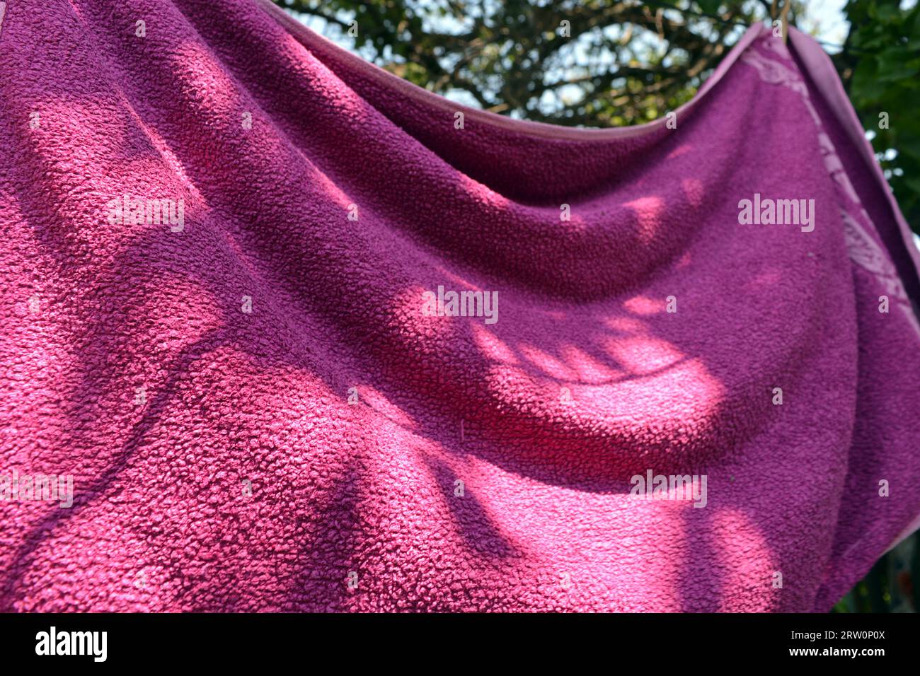 Towels of different colors and sizes are dried in the sunlight outside. The towels flutter in the wind and hang on a black glossy rope. Stock Photo