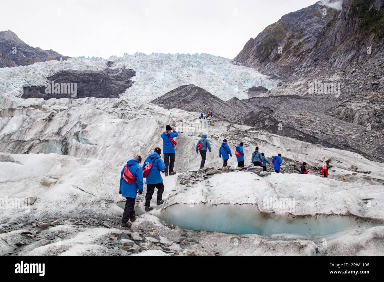 Franz Josef, New Zealand, March 22, 2015: A group of tourists hiking towards a helicopter on Franz Josef Glacier Stock Photo