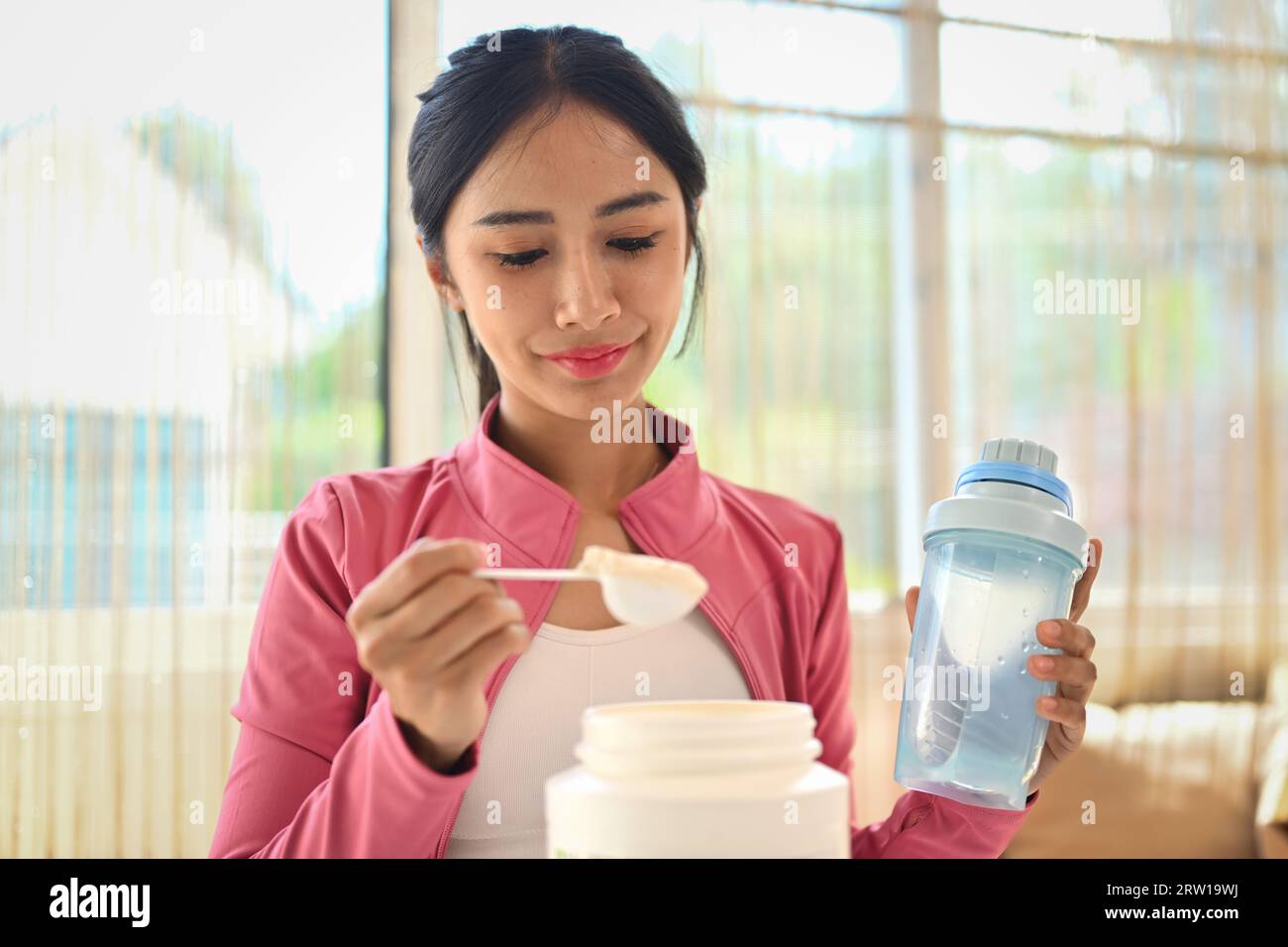 Young sporty woman measuring scoop of whey protein, making replacement