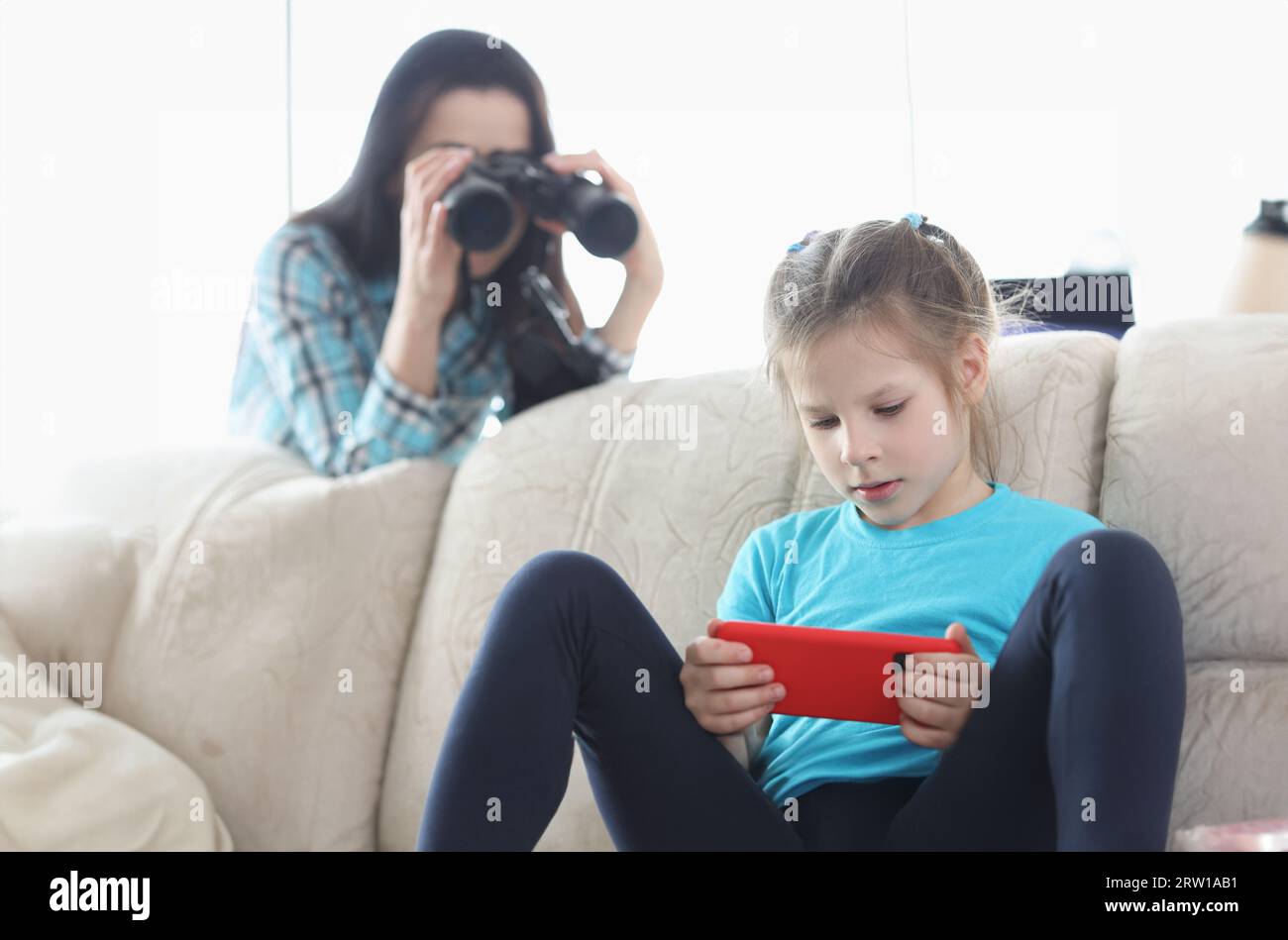 Mom controls her daughter with phone through binoculars Stock Photo