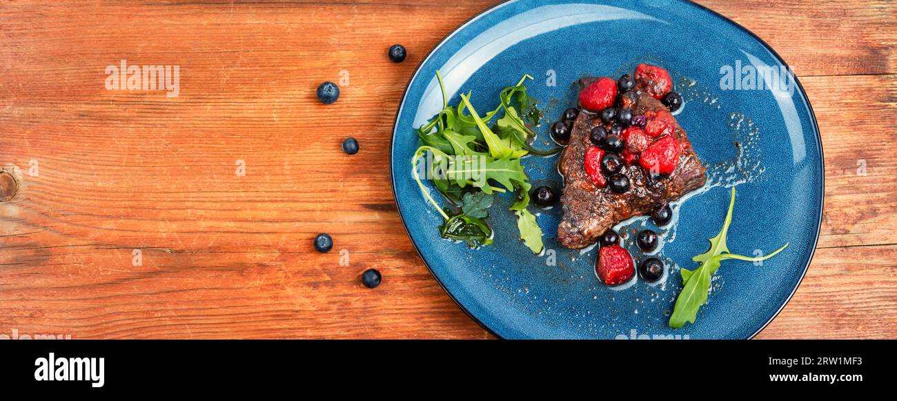 Delicious beef steak cooked with blueberry and raspberry sauce. Grilled meat medallions. Copy space, long banner. Stock Photo