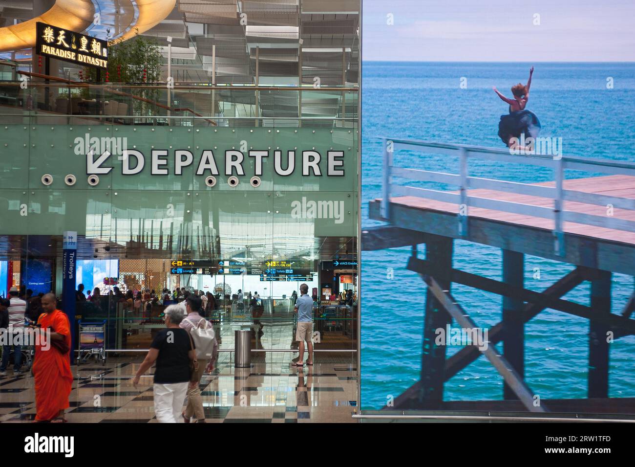 14.02.2018, Singapore, Republic of Singapore, Asia - Air travellers next to a huge digital billboard advert in the departure hall at Changi Airport T3. Stock Photo
