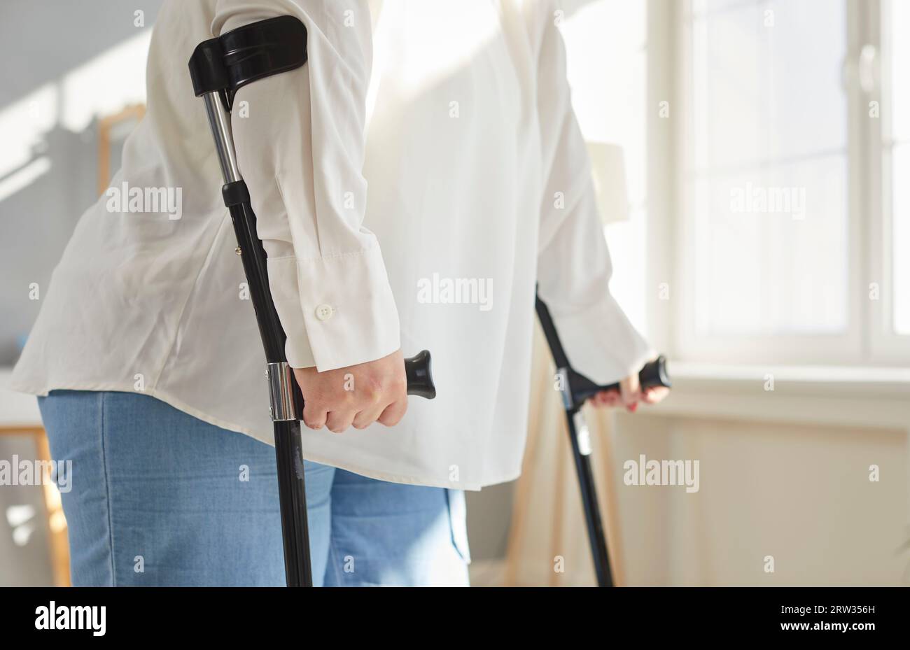 Cropped photo of a handicapped overweight fat woman with crutches trying to walk at home Stock