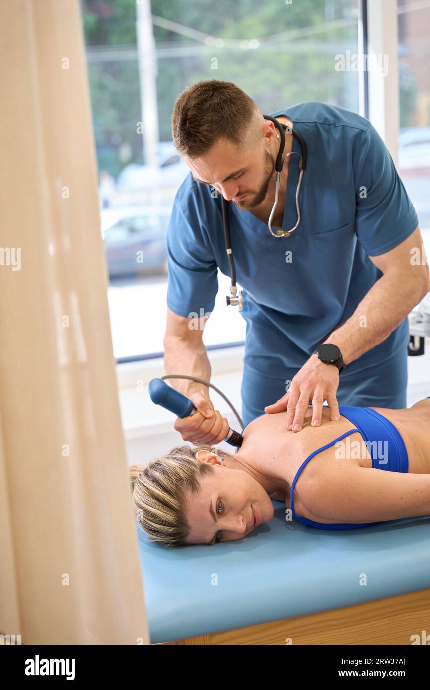 Rehabilitation specialist making extracorporeal shockwave therapy to woman Stock Photo