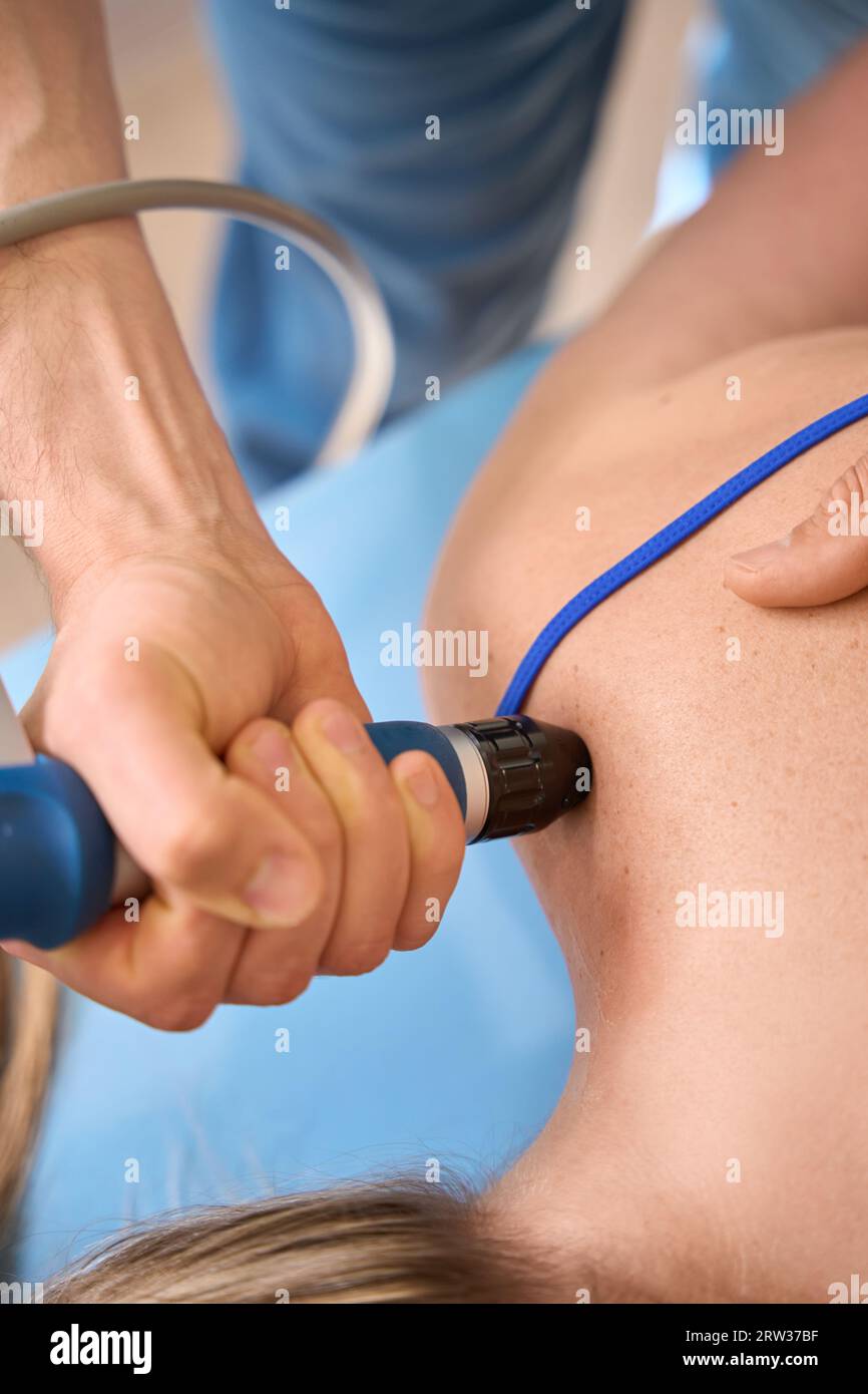 Male physiotherapist practicing extracorporeal shockwave therapy to female Stock Photo