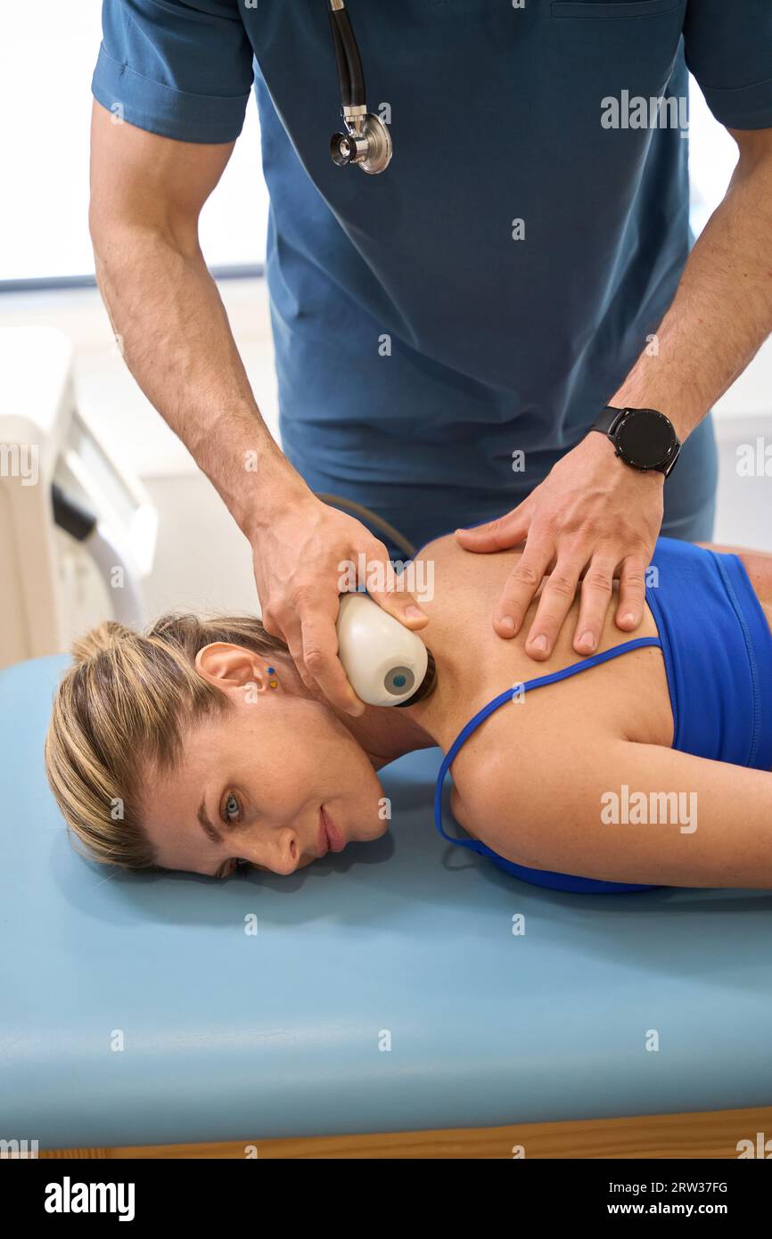 Male doctor conducting extracorporeal shockwave therapy to female patient Stock Photo