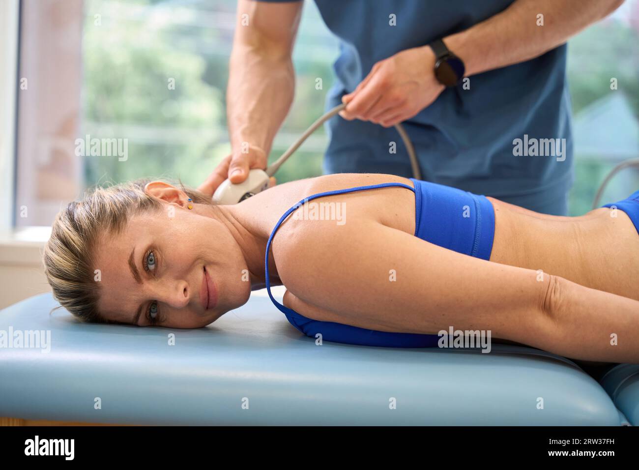 Smiling woman lying on massage couch during extracorporeal shock wave therapy Stock Photo