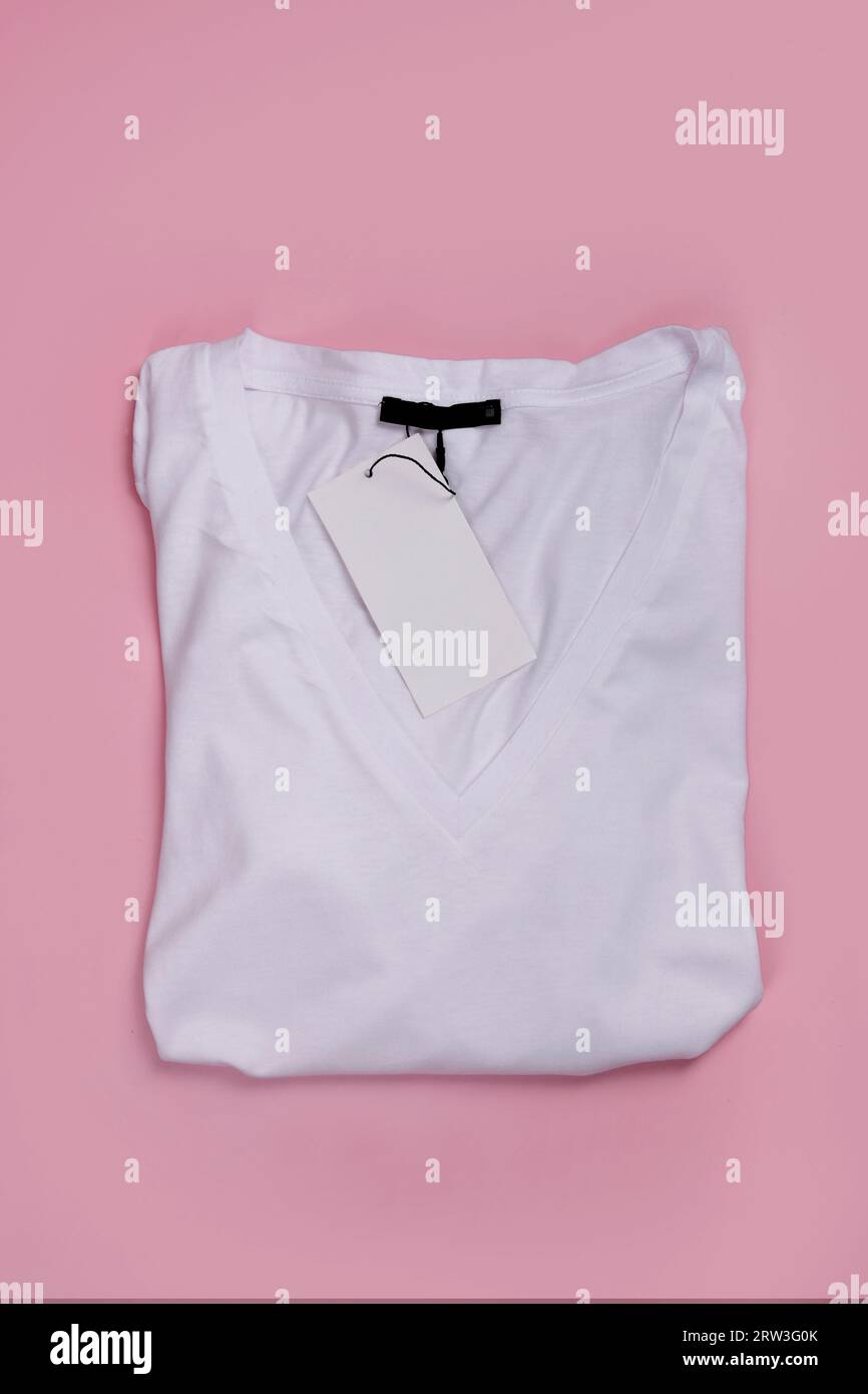 top view of white V-neck t-shirt folded with label on pink background Stock Photo